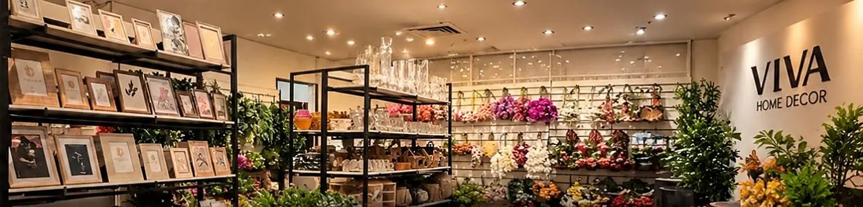 Interior da Viva Home Decor com estantes de quadros, taças, parede de flores permanentes e o letreiro da marca