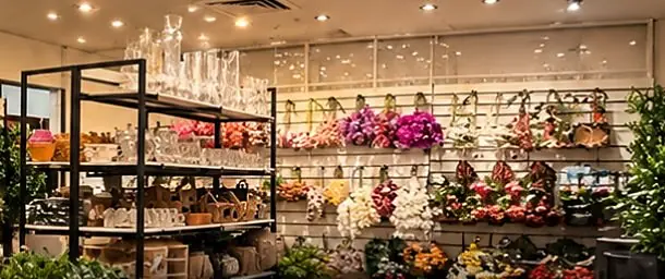Prateleiras com taças e peças de vidro diante da parede de flores da Viva Home Decor